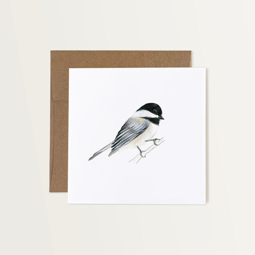 This note card features a hand-painted watercolor illustration of a chickadee on a white background. The bird has a black capped head with white and black wings and a white chest. It’s depicted perched on a branch. The greeting card is paired with a brown Kraft paper envelope.